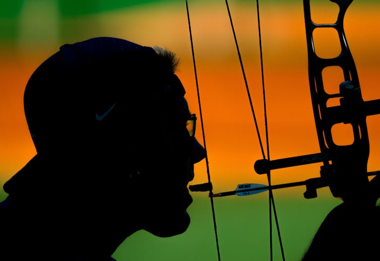 A disabled archer prepares to shoot by using his teeth to pull back the arrow.