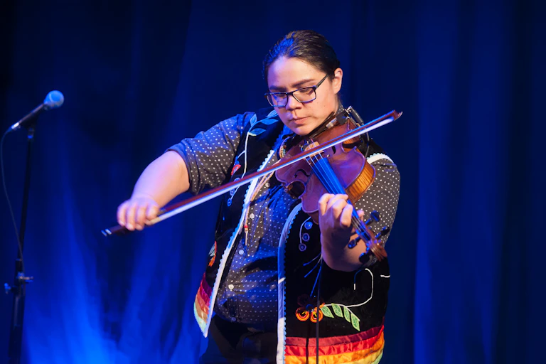 A person plays a fiddle on a stage in front of microphone.
