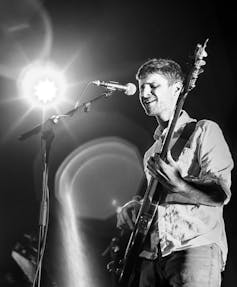 A musician holding a guitar and singing.