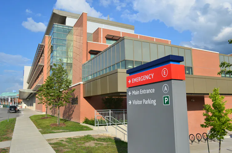 A sign in front of a hospital giving directions for the emergency entrance.