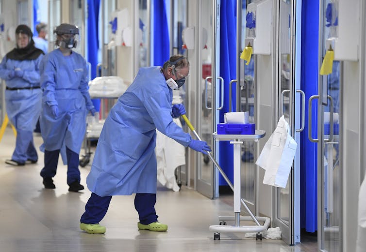 A man in personal protective equipment mopping a floor in a hospital ward.