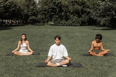Three people meditating in a park