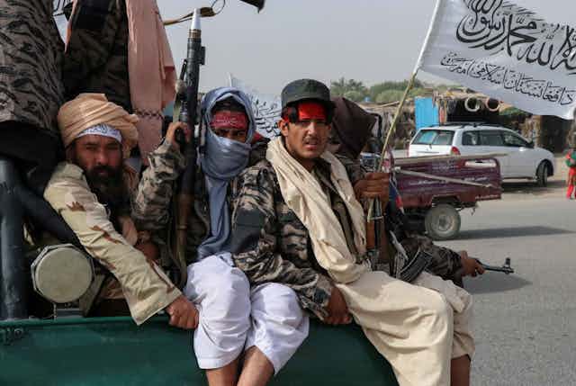 Combatientes talibanes sosteniendo armas y una bandera en la parte trasera de un camión. 