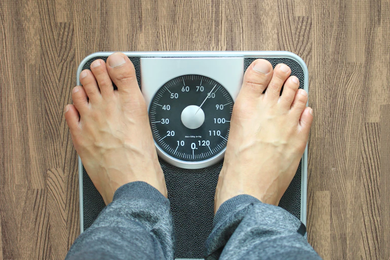 A person with bare feet stands on a scale to measure their weight.