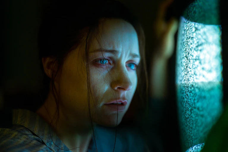 A woman looks at a staticky screen.