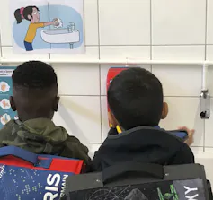 The backs of two children seen at a sink with a picture showing handwashing.