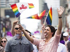 Justin Trudeau laughs and sticks out his tongue while waving a Pride flag.