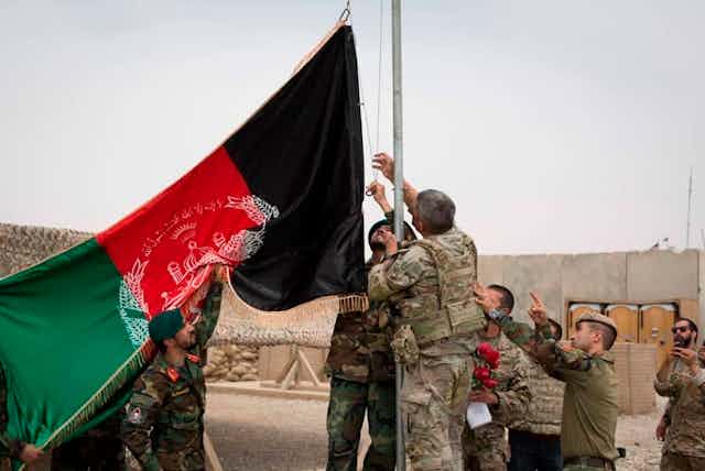 A group of people in military uniforms surround a flagpole with the Afghan flag