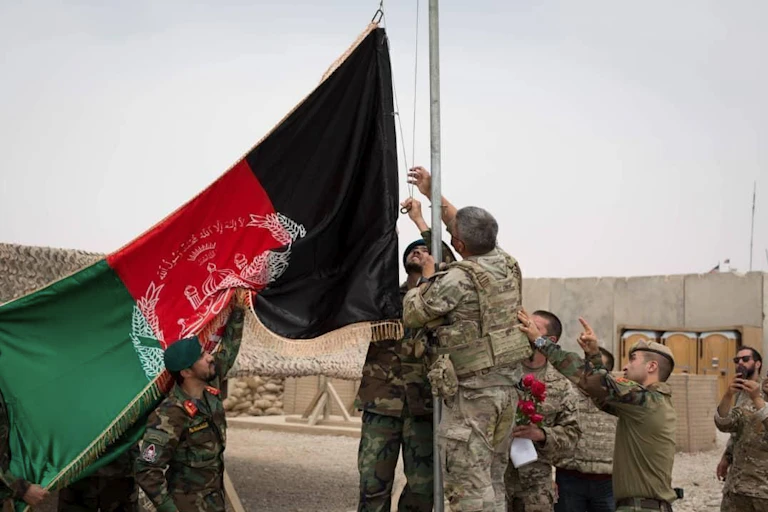 A group of people in military uniforms surround a flagpole with the Afghan flag