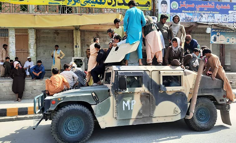 Men in civilian attire stand and sit atop a military vehicle