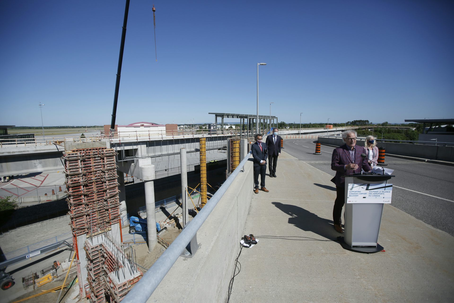 People stand at a podium during a press conference as building is taking place in the background