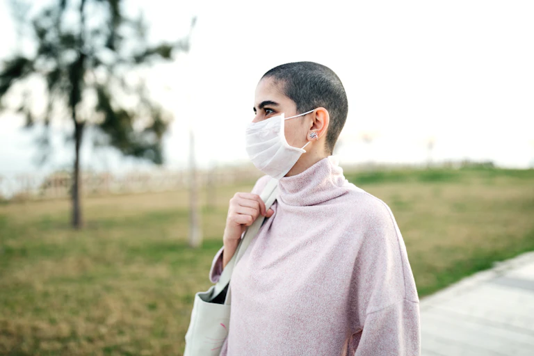 Bald person wearing mask outside.
