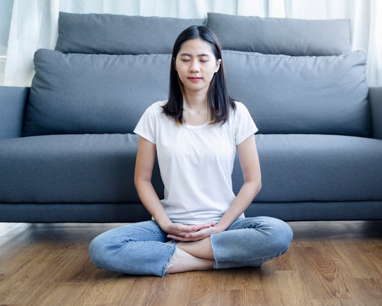 Young Asian woman sitting cross-legged on the floor with her eyes closed.