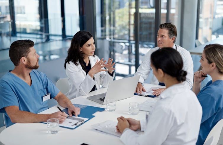 Group of five health care providers sitting around a table in discussion.