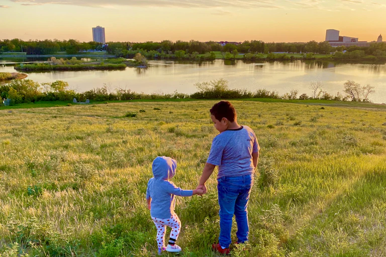 Two children hold hands looking at the water