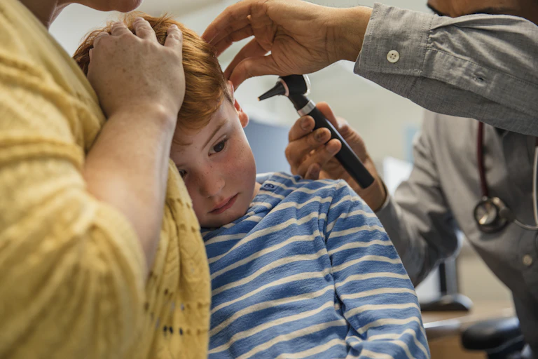 little boy being held by woman while clinician looks in his ear with otoscope