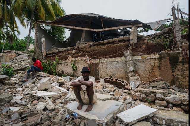 Un homme est assis devant les ruines de sa maison.