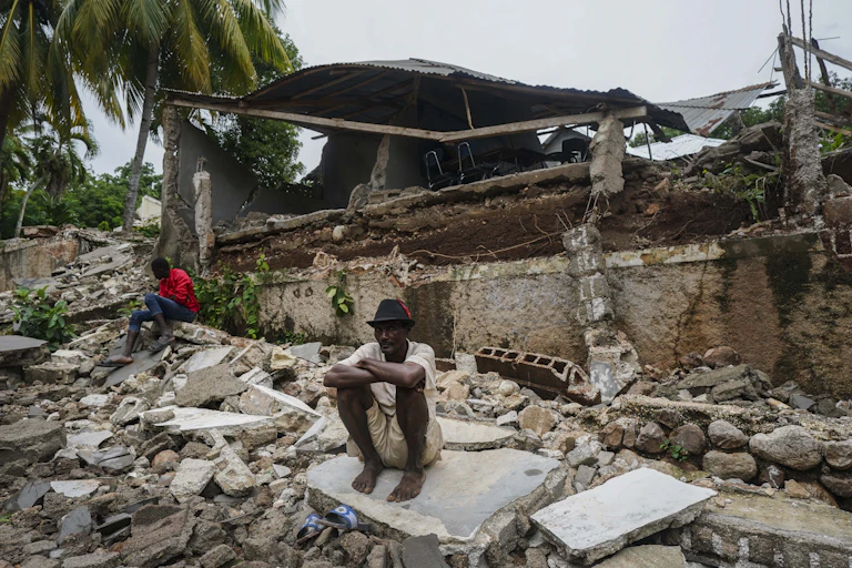 Un homme est assis devant les ruines de sa maison.