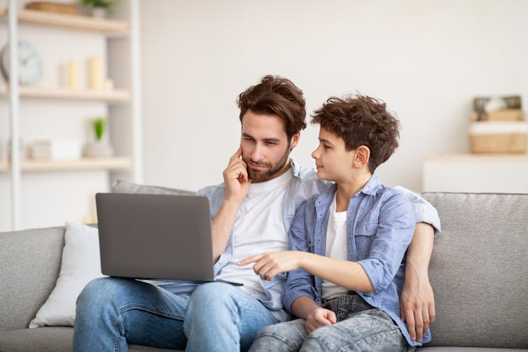 father and son seated on a couch discussing something on their laptop