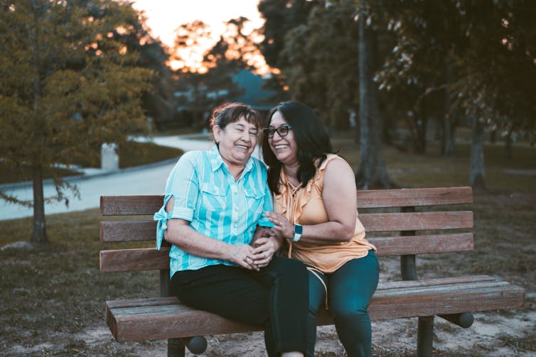 Two older women laughing on a bench