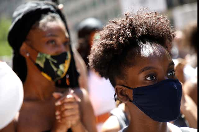 Black woman in a crowd wearing a mask and looking alert