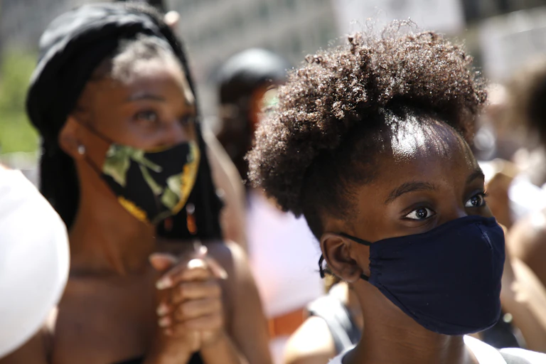 Black woman in a crowd wearing a mask and looking alert