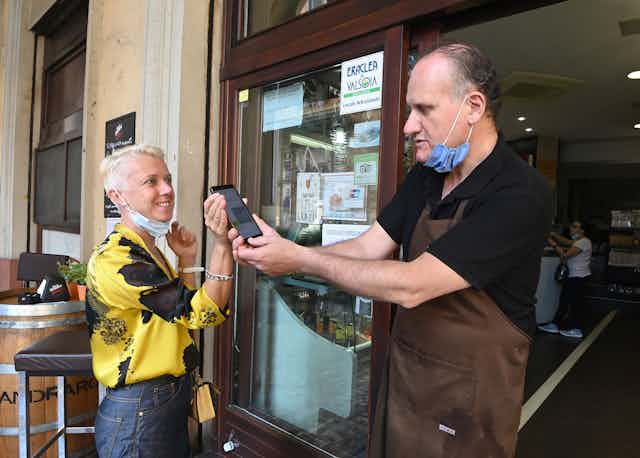 A customer shows the green pass to a staff member before entering the indoor dining area of a restaurant in Bologna, Italy, on Aug. 6, 2021.