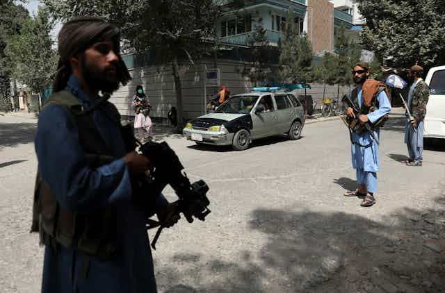 three afghani men holding machine guns stand in an urban street