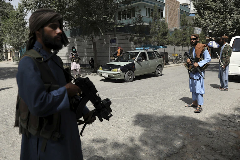 three afghani men holding machine guns stand in an urban street
