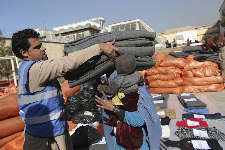 A UNHCR employee hands an Afghan woman sacks of supplies