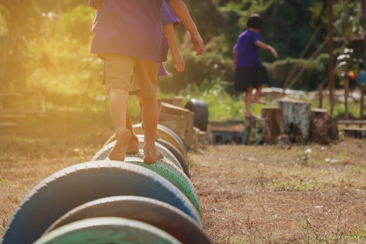 Kids walking on tyres in playground.