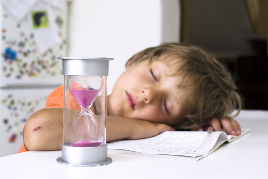 A young boy sleeping on his notebook, next to an hourglass that is emptying.