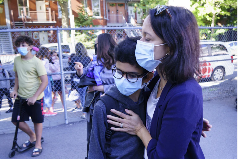 A mother embraces her son in a school yard, both wearing face masks.