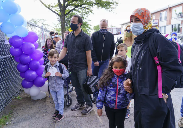 Parents in masks congregate with their children in a school yard.