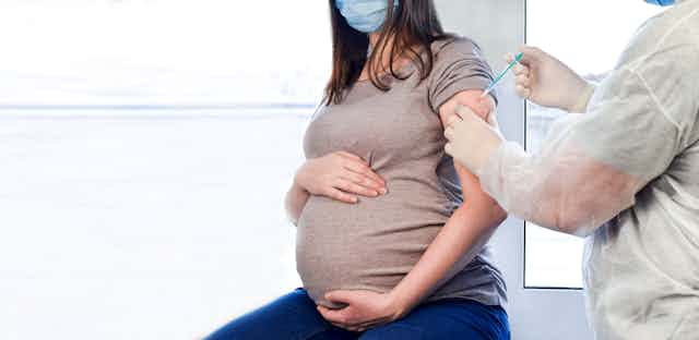 Pregnant woman in face mask being injected with COVID-19 vaccine