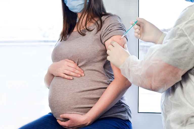 Pregnant woman in face mask being injected with COVID-19 vaccine