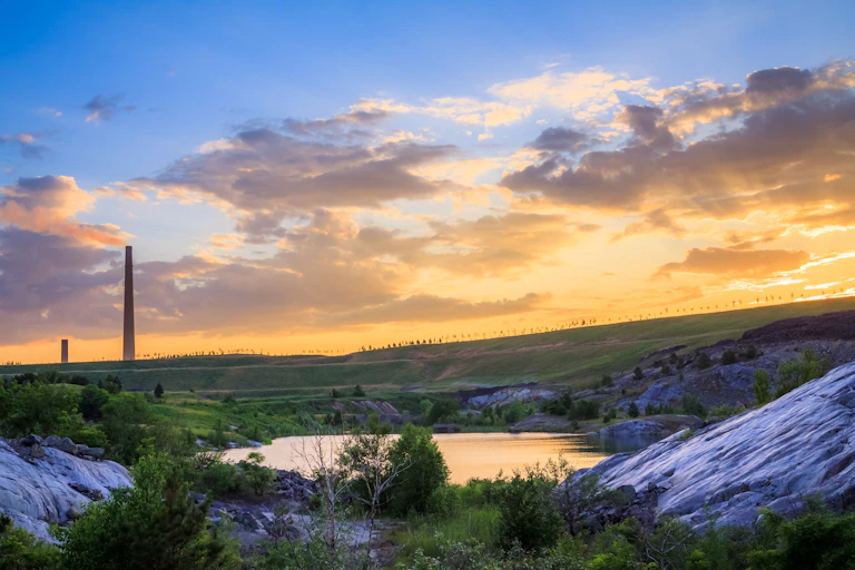 Two smoke stacks rising above treed hills in front of a lake.