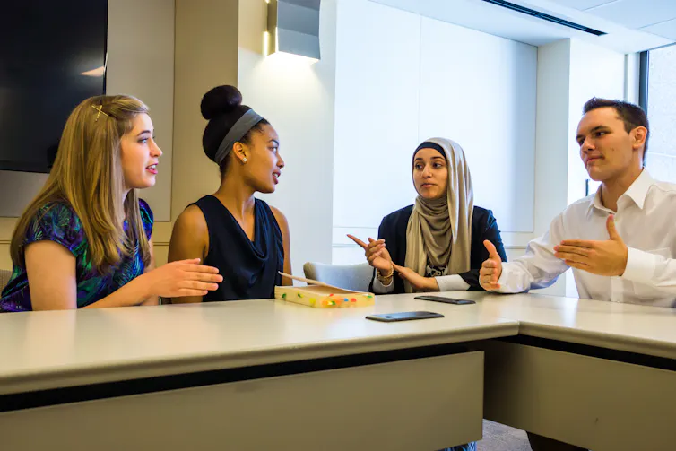 Four people have a discussion while siting around a table.