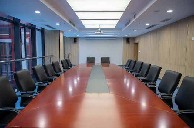 An empty board room with a reddish table and many leather seats around it
