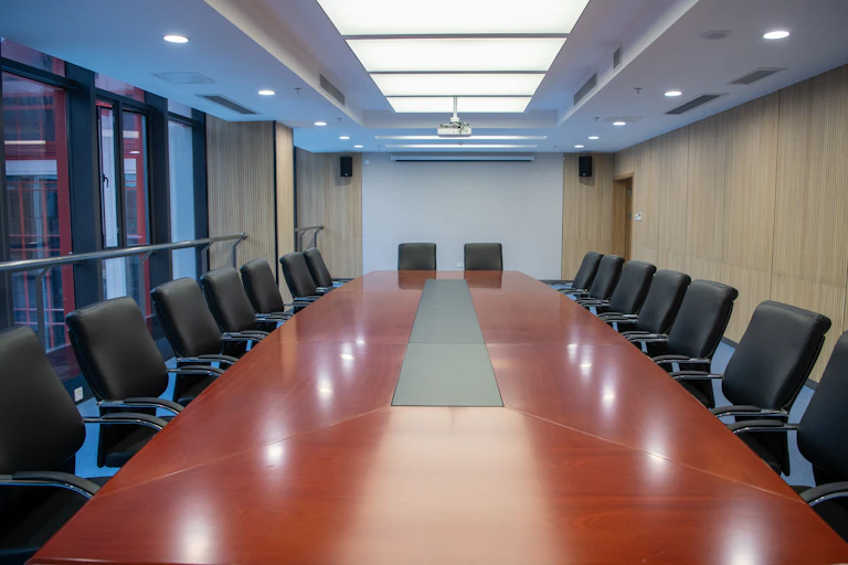 An empty board room with a reddish table and many leather seats around it