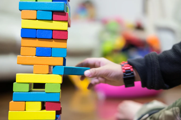 Kid pulling out Jenga block from tower about to fall.