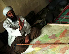 Osama bin Laden is shown sitting in front of a map.