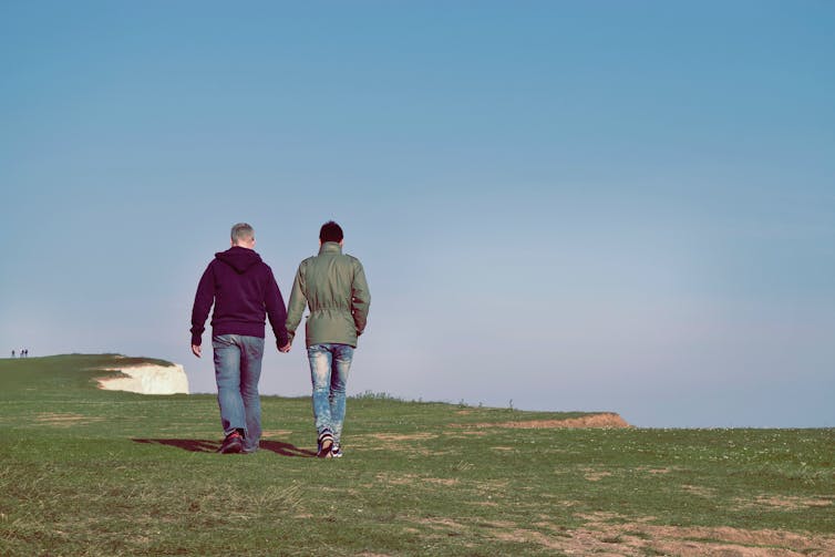 Two men hold hands while walking on grass