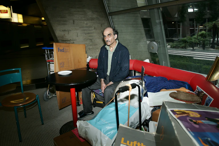 A man sits near his gear on a red bench in an airport terminal.