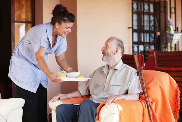 Aged care worker handing food to elderly resident