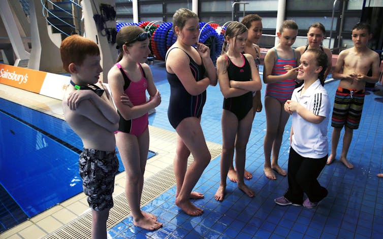Paralympian Ellie Simmonds stands with a group of children in swimsuits by a pool