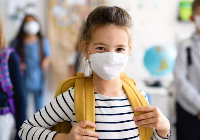 A young girl at school, wearing a backpack and a facemask