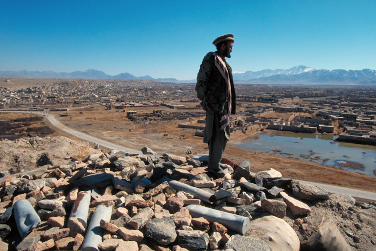 A Taliban figter looks across the land from atop a shell-littered peak.