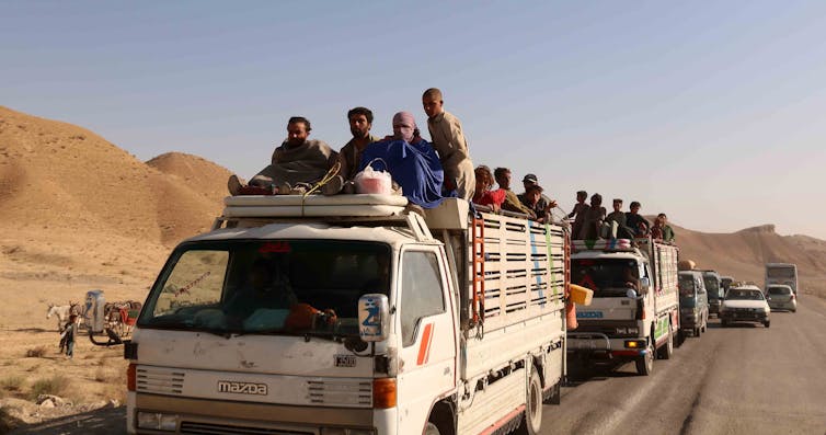 A convoy of trucks full of people and their belongings making its way down a highway in Afghanistan.
