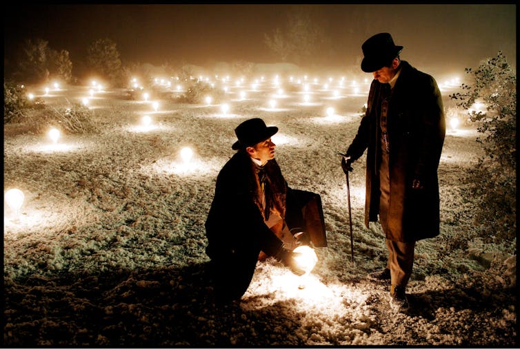Two men in a dark field lit up by light bulbs.